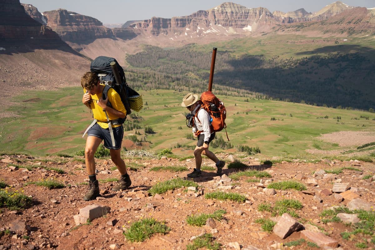 Two hikers with backpacks walking up a mountain trail